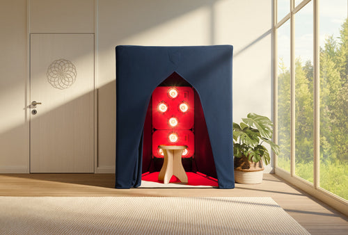 A compact SaunaSpace FireLight Infrared Sauna with glowing red lights and a wooden stool is set up in a bright room with large windows and a nearby potted plant.