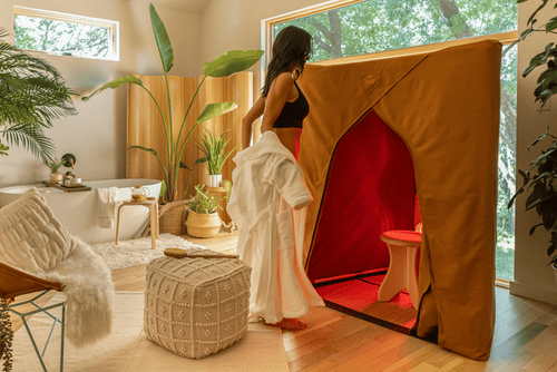 In a bright bathroom a woman removes her robe to enter a FireLight Sauna