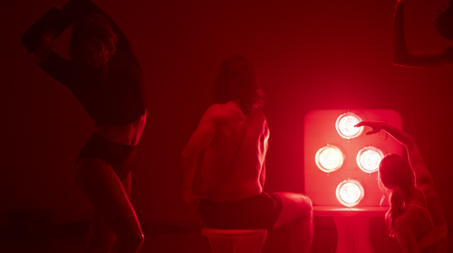 People moving and stretching in dark room in front of Hearth Quartet Infrared Therapy Panel