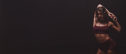 Woman stretching in dark yoga clothes against dark background