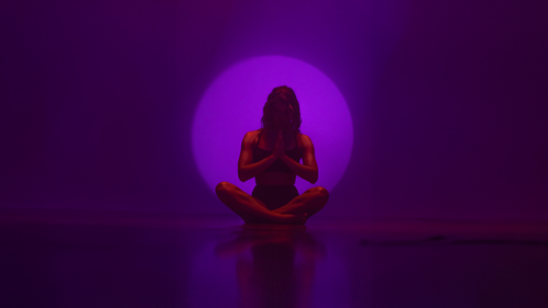 Woman seated in meditation pose in front of circle of violet light