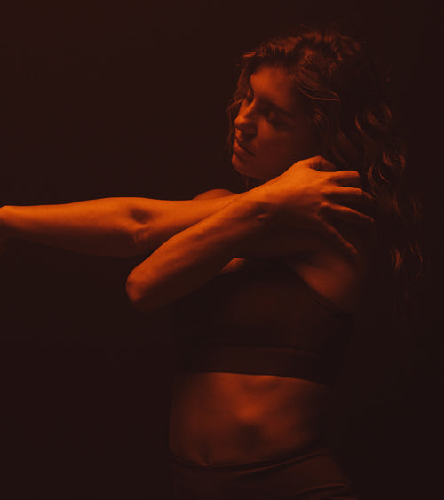 Woman stretching arm with eyes closed under dim red light