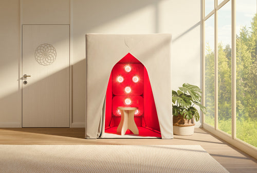 A beige SaunaSpace FireLight Infrared Sauna tent with red infrared lights and a small stool inside, placed near a potted plant in a bright, modern room with large windows.