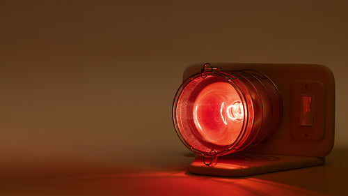 Glow Infrared Therapy Light sitting on protective basswood base with light on in dimly lit room with beige background.