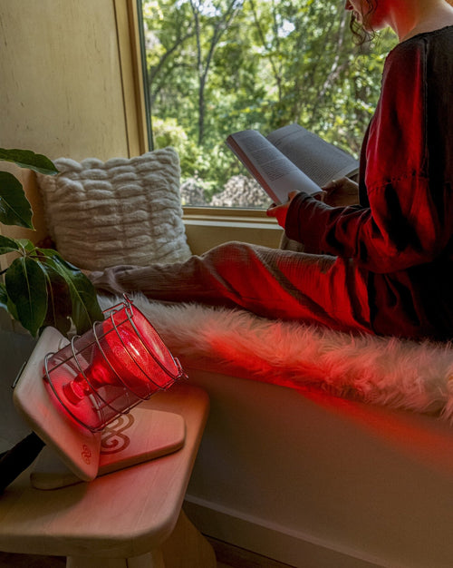 Woman reading in living room next to SaunaSpace Glow Infrared Therapy Light