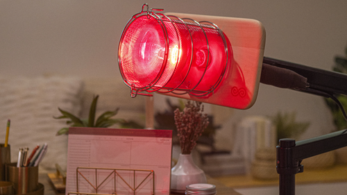 Glow Infrared Therapy Light mounted on Glow Desk Arm which is mounted on office desk with pens and papers and plants in background