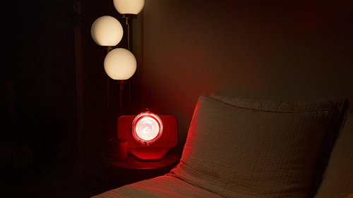Glow Infrared Therapy Light turned on and rested on night stand next to bed with globe lights above in dimly lit bedroom