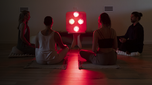 People seated in meditation on yoga mats and pillows in front of Hearth Quartet Infrared Sauna Panel seated on Pedestal in dimly lit room.