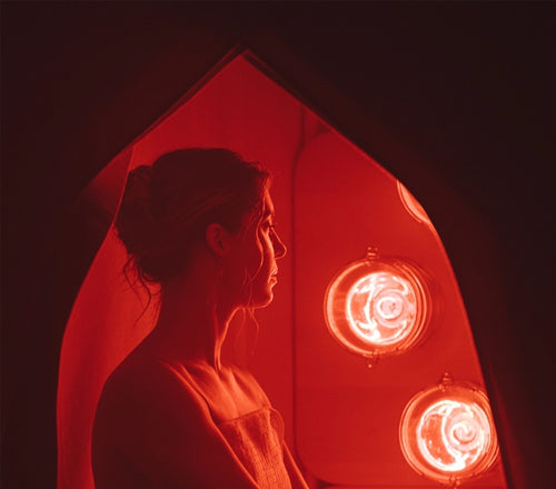 Silhouette of a woman sitting in FireLight Infrared Sauna with lights on against a dark background.