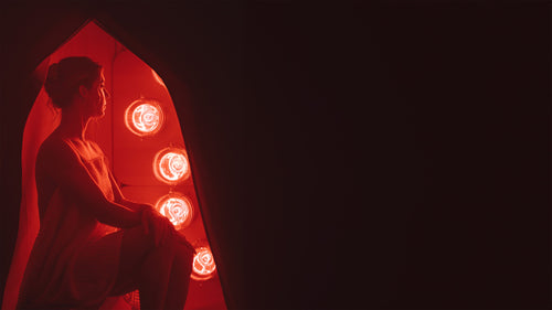 Silhouette of a woman sitting in FireLight Infrared Sauna with lights on against a dark background.
