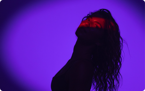 Silhouette of woman with red light on eyes against background of violet light.