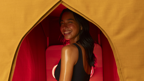 Woman smiling in FireLight Infrared Sauna - Turmeric with sauna entrance curtain open and lights on.