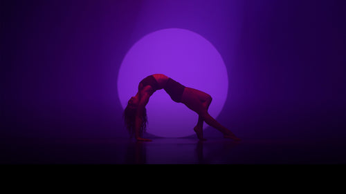 Person performing a backbend against a purple circular light on a dark background