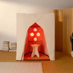 A FireLight Sauna set up in a bright living room with stacks of books on the left side. The FireLight Bulbs emit a warm, healing incandescent red light glow from within.
