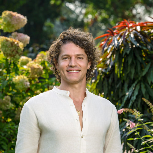 SaunaSpace Founder Brian Richards in a white linen shirt standing in a garden with greenery and flowers