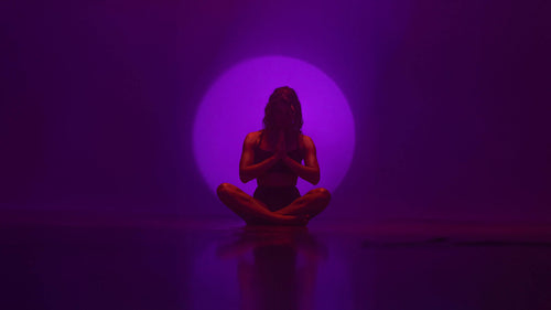 Woman seated in meditation pose in front of circle of violet light