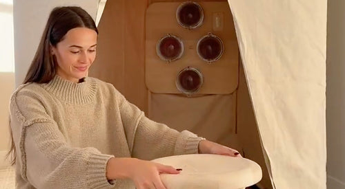 Woman in beige sweater holding sauna stool beside FireLight Infrared Sauna.