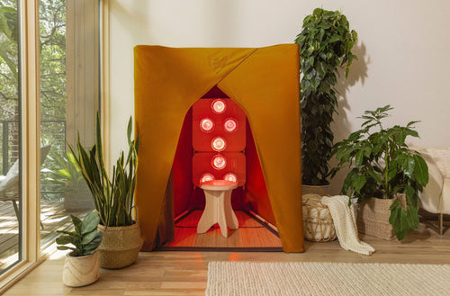 FireLight® Infrared SuperSauna in turmeric yellow, radiating red infrared light, set in a modern home living room with potted plants and wooden floors.