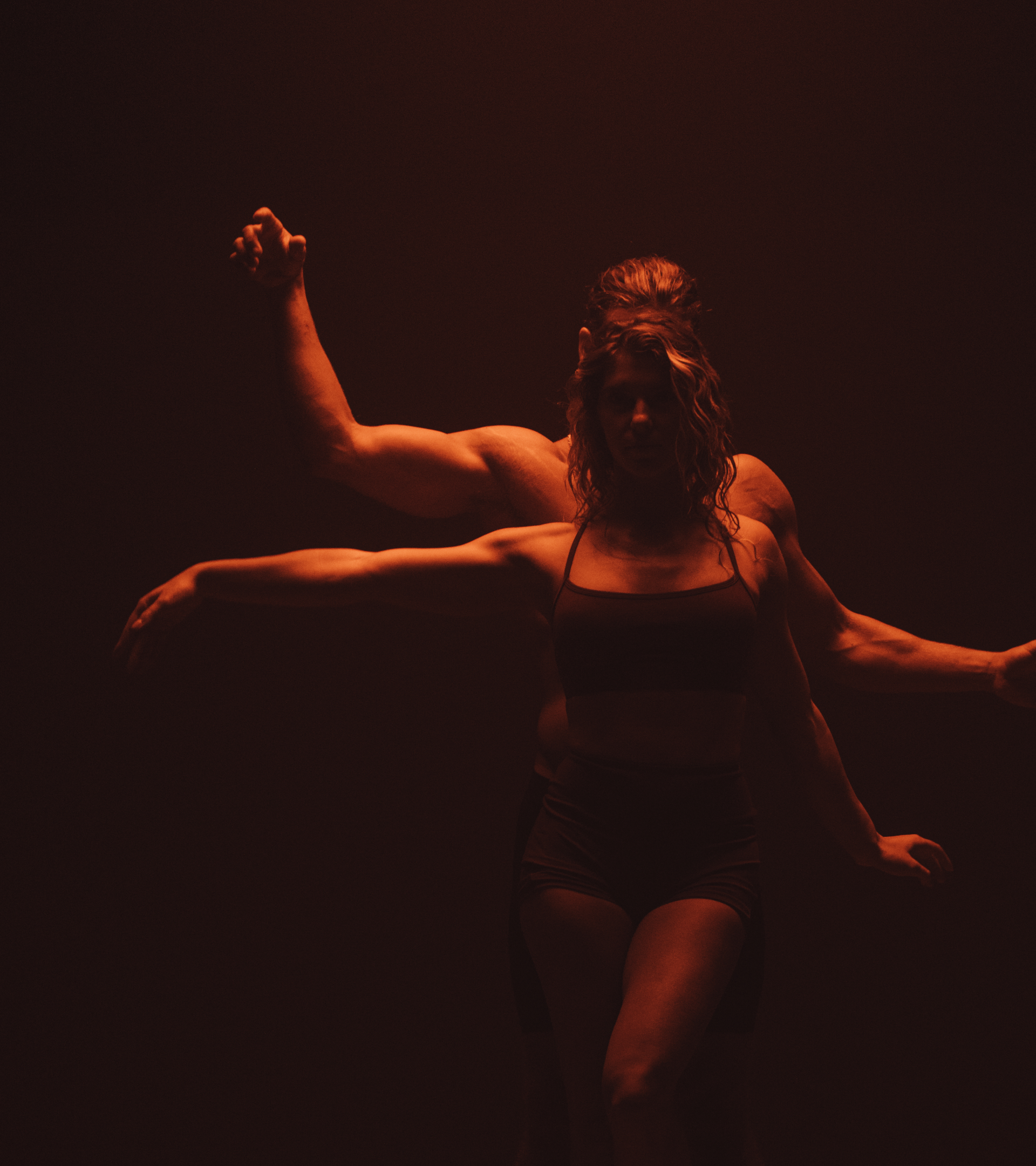 Dark scene of woman in front of man, each with arms raised in a dance