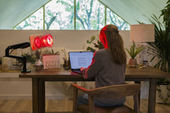 Woman sitting at desk with SaunaSpace Glow Desk Arm mounted on desk with Glow Infrared Therapy Light installed