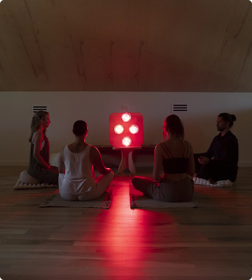 People seated in meditation on yoga mats and pillows in front of Hearth Quartet Infrared Sauna Panel seated on Pedestal in dimly lit room.