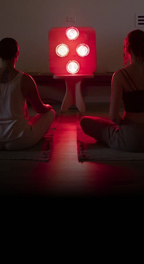 People seated in meditation on yoga mats and pillows in front of Hearth Quartet Infrared Sauna Panel seated on Pedestal in dimly lit room.