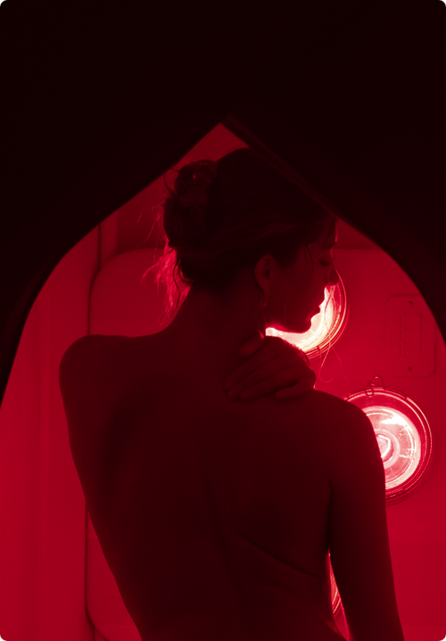 Woman with eyes closed sitting inside FireLight Infrared Sauna with sauna entrance curtain open and lights on