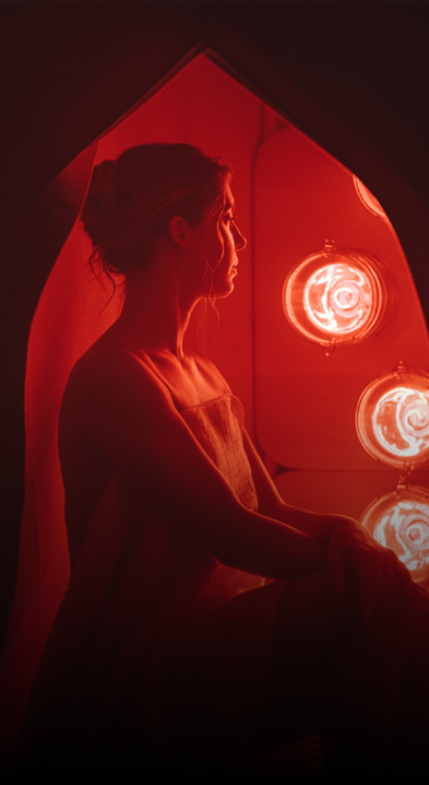 Woman sitting in FireLight Infrared Sauna on Sauna Stool with lights on and sauna entrance curtain open