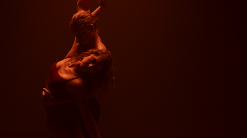 Man dancing with and holding woman in a dark glow of red light