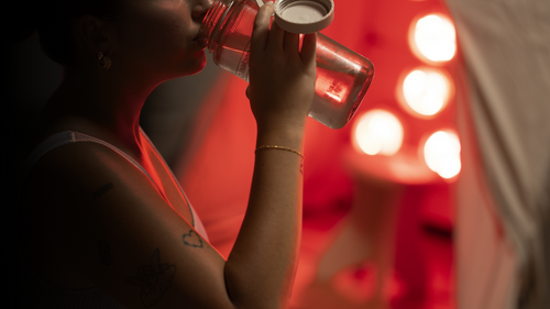 Woman drinking filtered water from bottle in preparation for her FireLight Infrared Sauna session
